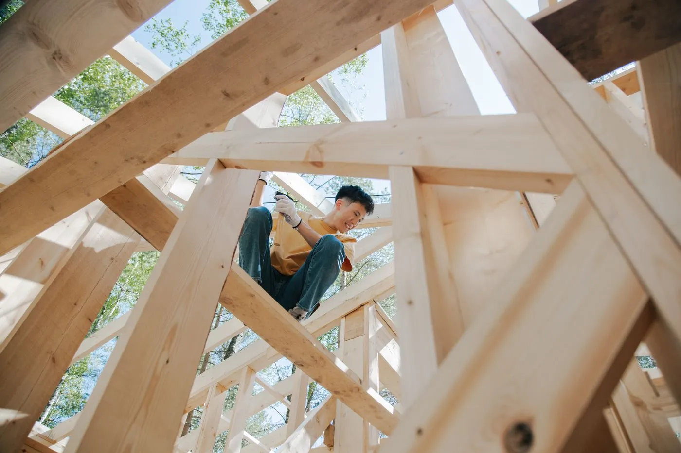 Carpenter fastening timber framing on a build, seen from below through the structure